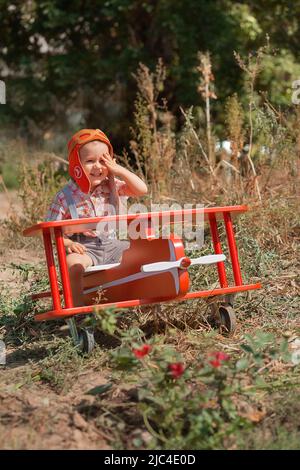 Happy kid boy pilot sitting and playing with toy red airplane on summer. Dreams child of travel Stock Photo