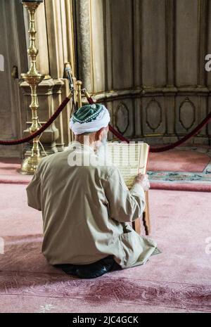 Old man reading Quran in a mosque on display Stock Photo