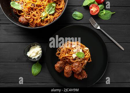 Homemade pasta with tomato sauce. Italian spaghetti with meat balls on a black plate on a wooden black background. With the ingredients for cooking Stock Photo