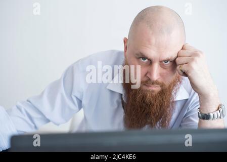 A focused bald man with a red beard stares intently at the camera. Male manager in a white shirt is angry at work. Stock Photo