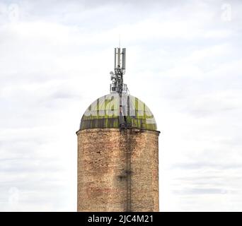 An old brick tower with weathered metal roof and wireless communication antenna transmitter against cloudy sky and. Internet, 3G, 4G and 5G cellular connection. Stock Photo