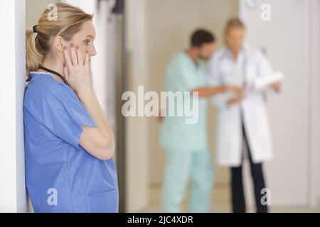 sad nurse leans against wall in hospital corridor Stock Photo