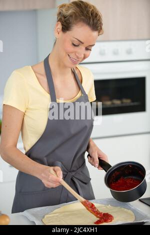 woman wearing apron standing in kitchen making pizza Stock Photo