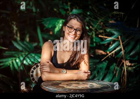 beautiful young Latina woman sitting at a table with jungle type background Stock Photo