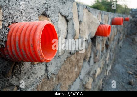 A row of orange culverts or water outlet pipes through a stone retaining wall for storm drainage in the hills of Uttarakhand India. Stock Photo