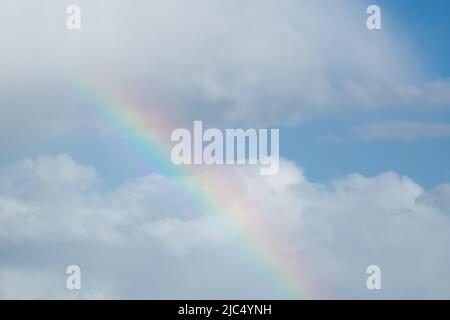 Colorful rainbow against bright clouds and blue sky, abstract background Stock Photo