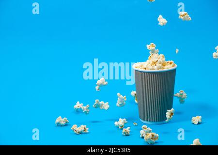 Popcorn is poured into a paper brown glass on a blue background with place for text. Stock Photo