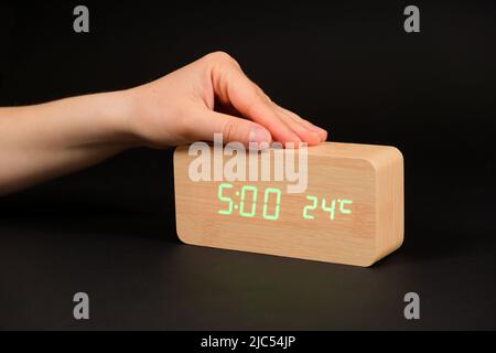 A digital clock showing a time of five o'clock in the morning and a woman's hand on a black background Stock Photo