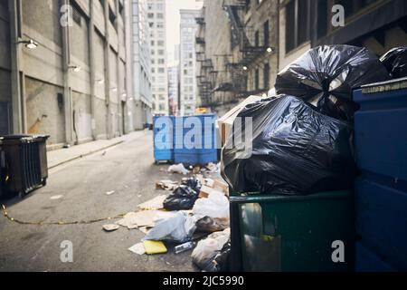 Mess and full garbage cans in narrow alley amidst buildings in city. Stock Photo