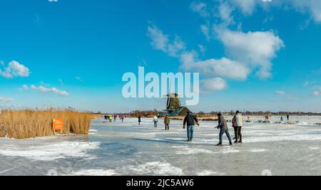 Scating on a frozen canal near a windmill *** Local Caption ***  Netherlands,windmill, water, winter, snow, ice, people, scaters,  ,Westzaan,   Noord- Stock Photo