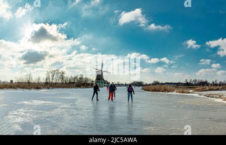 Scating on a frozen canal near a windmill *** Local Caption ***  Netherlands,landscape, water, winter, snow, ice, people, scaters,  ,Westzaan,   Noord Stock Photo