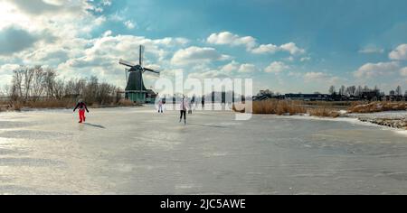 Scating on a frozen canal near a windmill *** Local Caption ***  Netherlands,landscape, water, winter, snow, ice, people, scaters,  ,Westzaan,   Noord Stock Photo