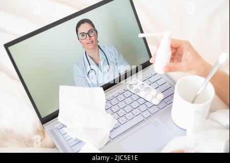 A woman lies in bed and holds a spray for sore throat. A friendly doctor talks to a sick patient by video link. Therapist on a laptop screen. Online Stock Photo