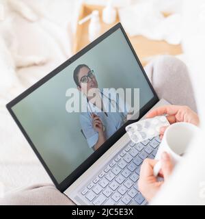 A woman lies in bed and holds a spray for sore throat. A friendly doctor talks to a sick patient by video link. Therapist on a laptop screen. Online Stock Photo