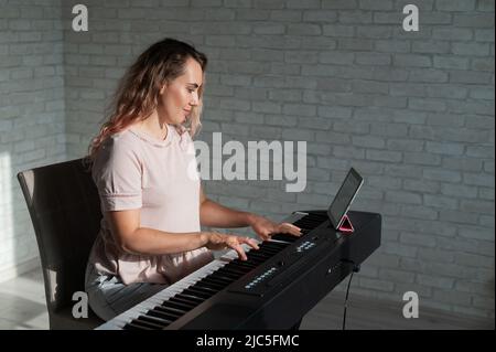 Caucasian woman remotely teaches electric piano playing via video communication on a digital tablet Stock Photo