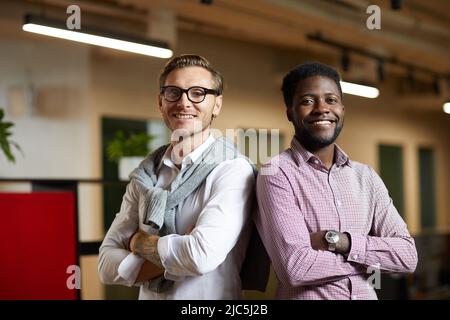 Positive confident young multi-ethnic startuppers standing back to back and looking at camera in office Stock Photo
