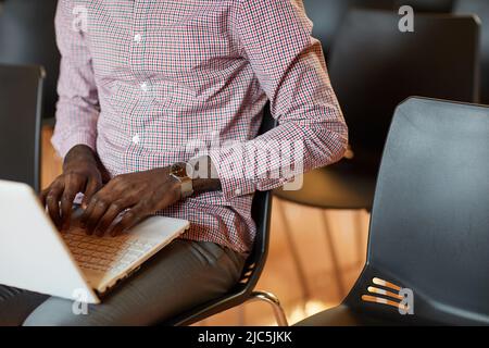 Close-up of unrecognizable Black man with wristwatch sitting on chair and composing business article on laptop Stock Photo