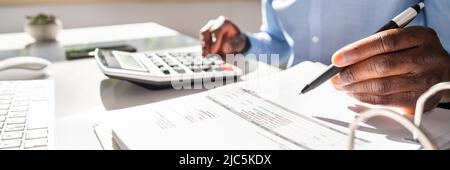 Happy Young Businessman Calculating Invoice On Computer Screen Near Laptop Stock Photo