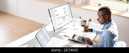 Side View Of Young Businessman Calculating Invoice On Computer Screen Near Laptop Stock Photo