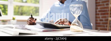 Hourglass In Front Of Businessperson Calculating Invoice Stock Photo