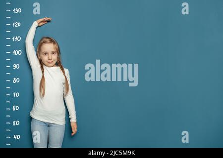 Kid girl measures the growth on blue background. Education and grow up concept Stock Photo