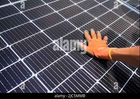 Close up of man solar technician installing solar modules for generating electricity through photovoltaic effect. Male hands in work gloves assembling photovoltaic solar panels. Stock Photo