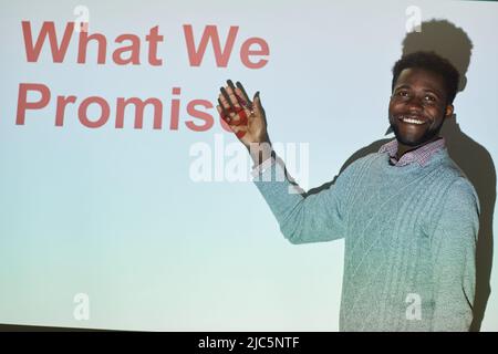 Positive handsome young Black businessman in sweater standing by projection screen and presenting marketing project Stock Photo