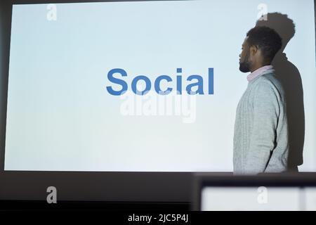 Pensive young Black SMM specialist in sweater standing at projection screen and explaining marketing plan at training class Stock Photo