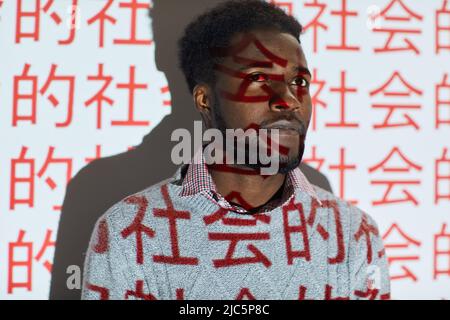 Pensive young African-American man in sweater standing against projection screen with hieroglyphs while studying Chinese language Stock Photo