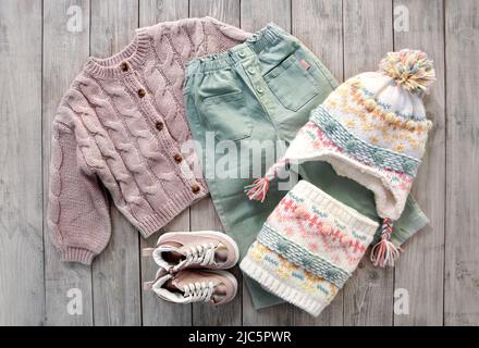 Child's girl knitwear set on wooden background flat lay. Kid's winter woolen clothes top view. Toddler knitted cardigan,pants,hat and shoes. Collectio Stock Photo