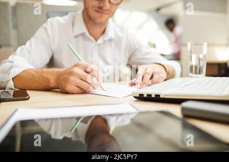Close-up of young man sitting at table and drawing scheme on paper while working on design of project Stock Photo