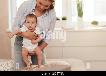 Young mother holding her adorable little baby girl in white bodysuit when they are spending weekend at home Stock Photo