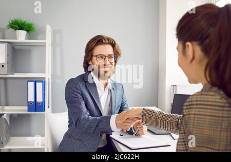 Friendly man shakes hands with woman during interview and congratulates her on getting new job. Stock Photo