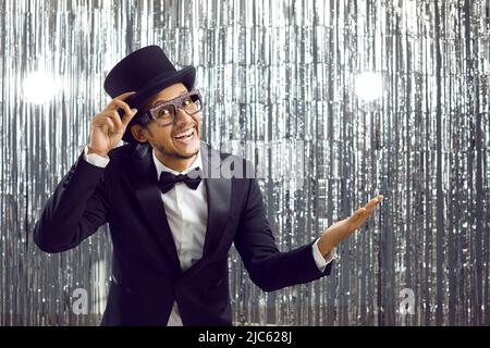 Happy smiling man in suit, top hat and glasses presents something on blank background Stock Photo