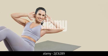 Young sporty woman practicing exercises for upper and lower abs isolated on beige background. Stock Photo