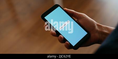 a man indoors is searching the text long covid in a simulated internet search engine in his smartphone, in a panoramic format to use as web banner or Stock Photo