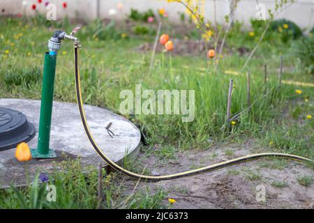 Plumbing, water pump from a well. An outside water faucet with a yellow garden hose attached to it. Irrigation water pumping system for agriculture. H Stock Photo