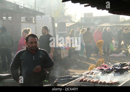 Farmers' market in a small village in Romania. Man preparing the traditional 'mititei' on the grill. Stock Photo