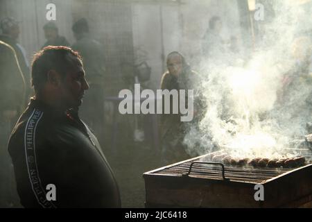 Farmers' market in a small village in Romania. Man preparing the traditional 'mititei' on the grill. Stock Photo