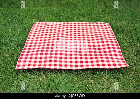 Red checkered gingham cloth on green grass. Picnic towel.Tabletop advertisement design. Food promotion display. Laying napkin. Stock Photo