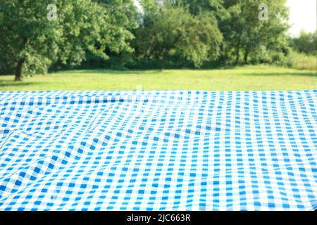 Blue checkered blanket on grass field natural background. Food advertisement display. Product promotion backdrop. Picnic cloth lying down outdoors. Stock Photo