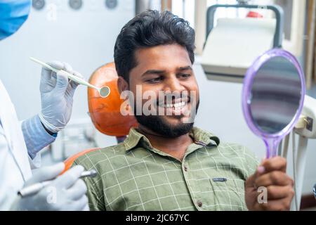 Happy smiling patient watching mirror after teeth treatment or oral cleaning at hospital - concept of dental care, treatment and happy client Stock Photo