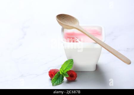 Raspberry yoghurt closeup empty copy space.Pink milky yogurt in plastic on table with berries. Stock Photo