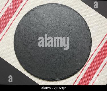 Slate black round dish empty space on dark background decorated with dish cloth.Tableware,sushi plate. Stock Photo