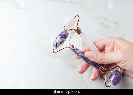 Female hand holding Rose quartz and amethyst face rollers for beauty facial massage therapy. Skin care tool for massaging morning routine. Luxury prod Stock Photo