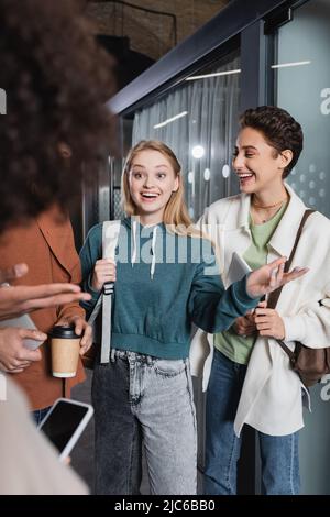 smiling woman pointing with hand while talking to multicultural students in university Stock Photo