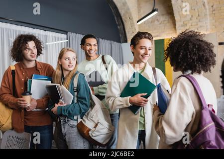 smiling multiethnic students with backpacks and notebooks talking in university Stock Photo
