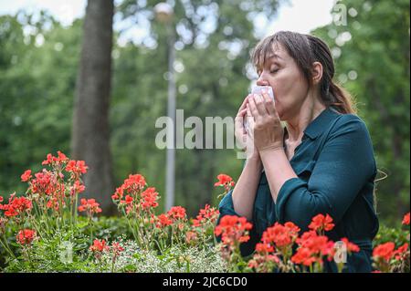 portrait of a girl in a blooming garden. Front view of lonely girl sneezing and blowing. Stock Photo