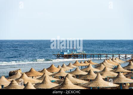 Red Sea and beach with straw umbrellas near Marsa Alam, Egypt, Africa. Seascape and waves breaking on the coral reef. Stock Photo