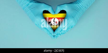 Doctors hands wearing blue surgical gloves making hear shape symbol with uganda flag Stock Photo